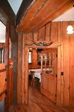 Rustic wood-paneled interior featuring exposed wood beams, wood-finish flooring, and a solid wood door with glass paneling