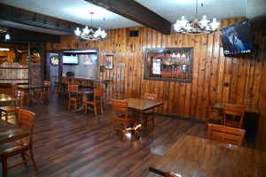 Interior space featuring wood-finish flooring, wood paneling, exposed ceiling beams, and two multi-bulb chandeliers
