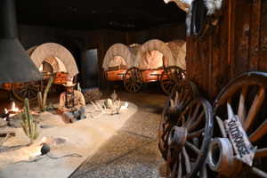 Themed interior space featuring multiple covered wagons with wood wheels, a faux campfire display, and an accent wall of wood planking
