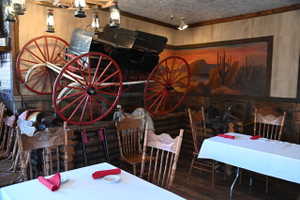 Interior dining area featuring wood-finish flooring, a wagon wheel ceiling fixture with lantern-style lighting, and a desert landscape mural