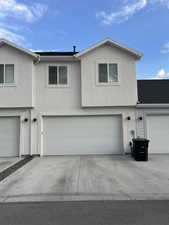 Stucco exterior with a pitched roofline, featuring two attached garage doors, concrete driveways, and upper-level windows