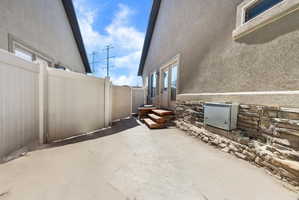 Private patio area featuring a light-colored privacy fence and stucco exterior with a stone veneer foundation