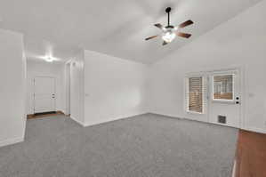 Spacious living room featuring vaulted ceilings, a ceiling fan with integrated lighting, and light gray carpeting