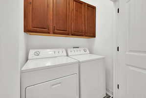 Dedicated laundry area featuring upper wood-finish cabinetry, and white paneled doors