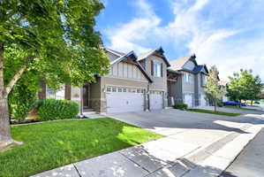 Contemporary exterior with a two-car garage, stone facade accents, decorative gable brackets, and mature landscaping
