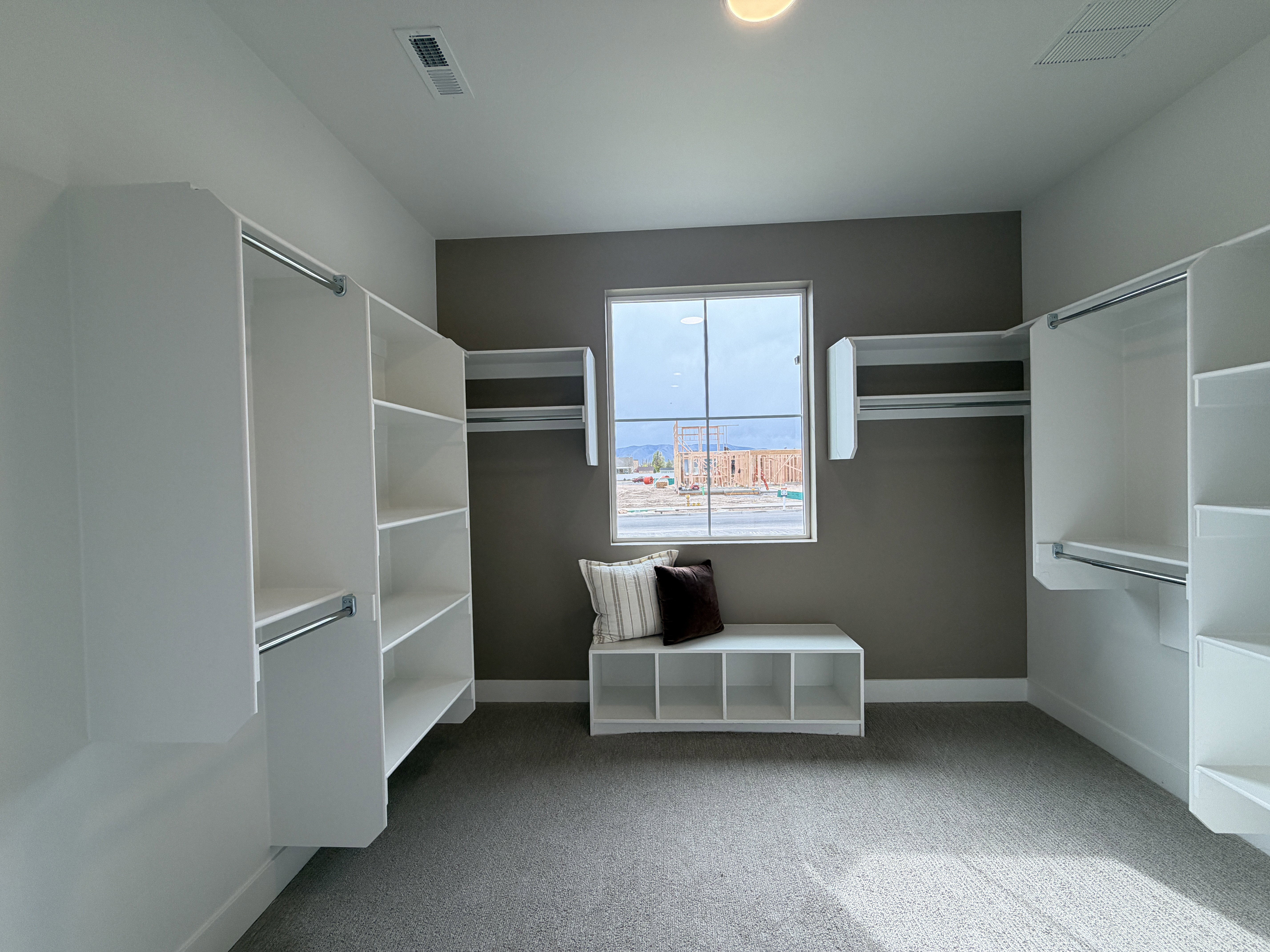 Spacious closet with ample white built-in shelving, multiple hanging rods, and a window for natural light