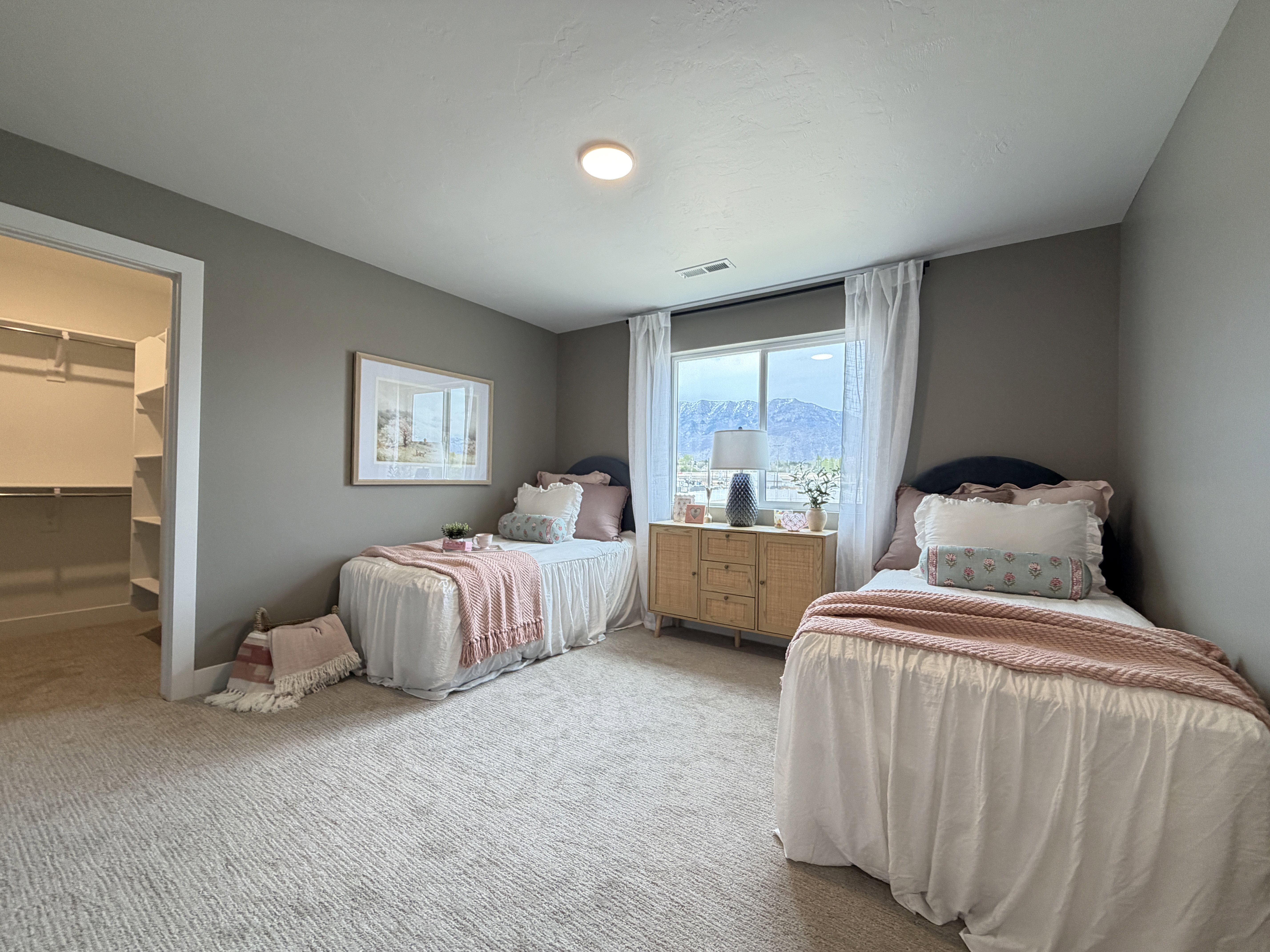 Spacious room featuring neutral carpeting, a large window with white curtain panels, and a built-in closet with shelving