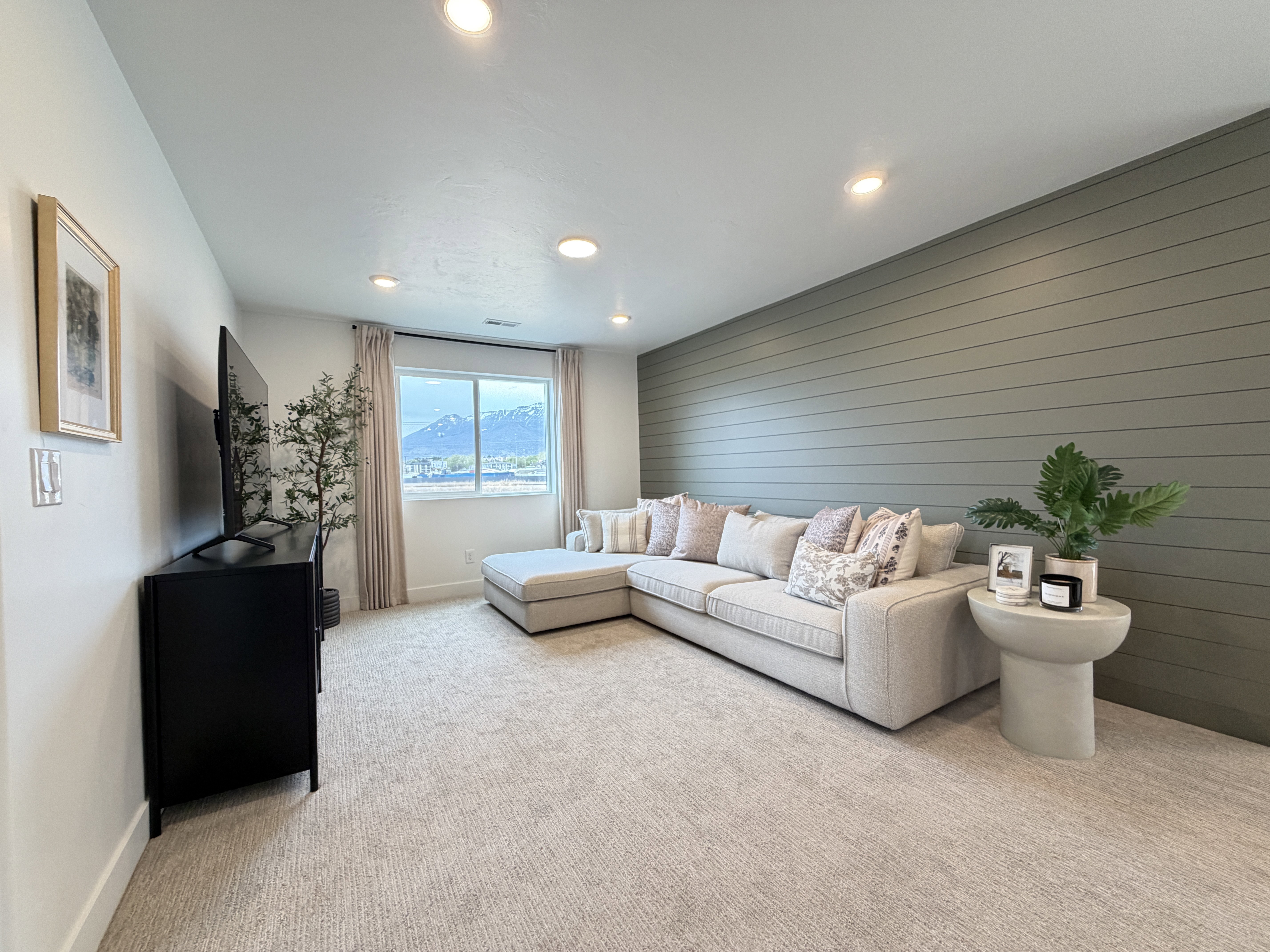 Spacious room featuring recessed lighting, a prominent horizontal shiplap accent wall, light-colored carpeting, a large window, and mountain scenery