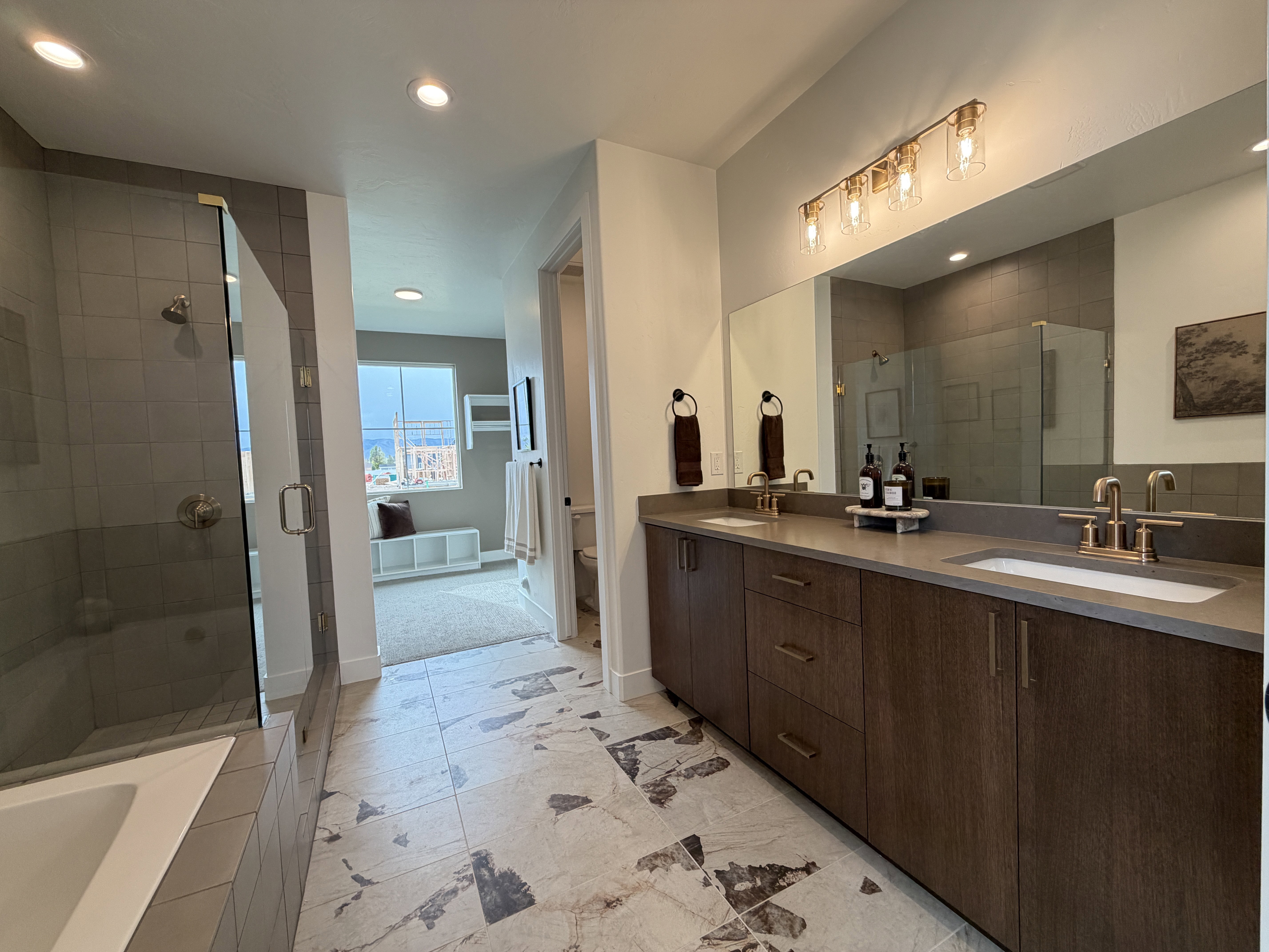 Spacious bathroom featuring a dual vanity with wood-finish cabinetry, a large integrated mirror, and bronze fixtures