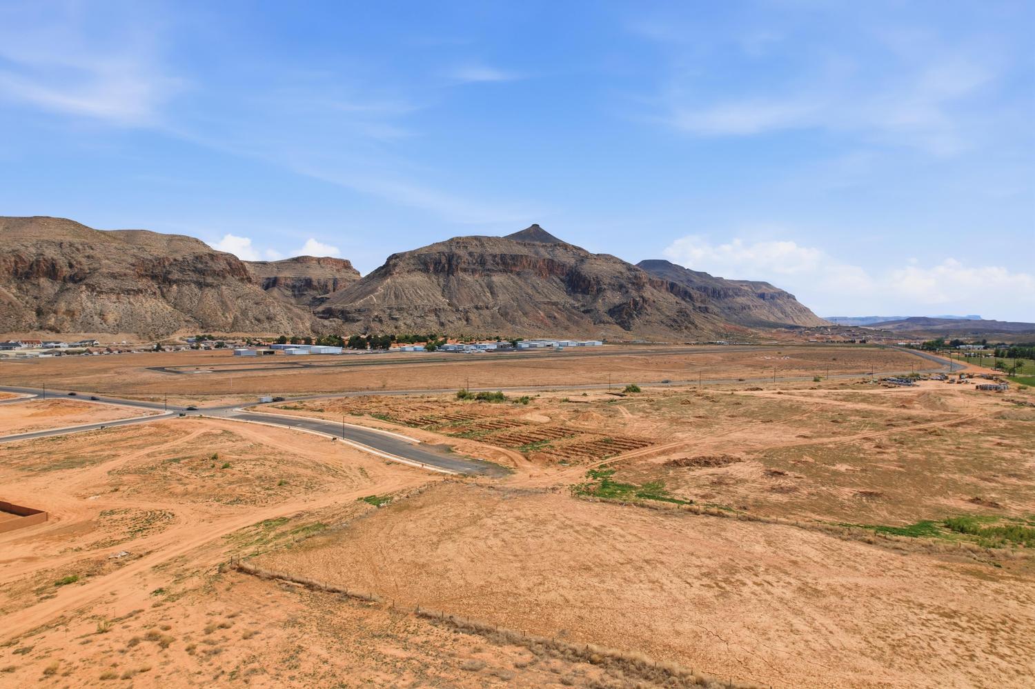 Expansive land parcel featuring existing paved roads and utilities visible in the distance, set against a backdrop of rugged mountains