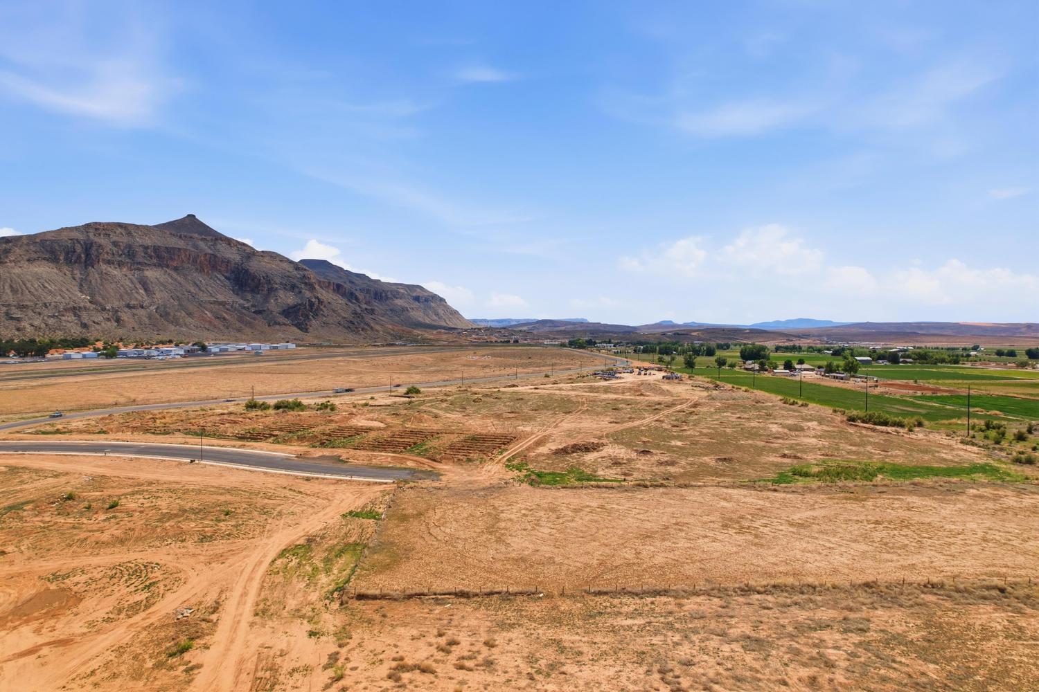 Expansive undeveloped land featuring a paved road, mountain backdrop, and distant green fields