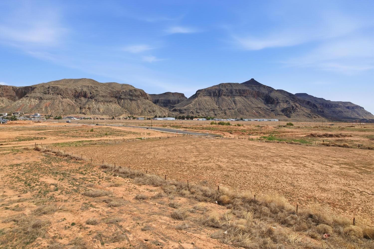 Expansive vacant lot featuring a dirt road, partial fencing, and distant mountain backdrops