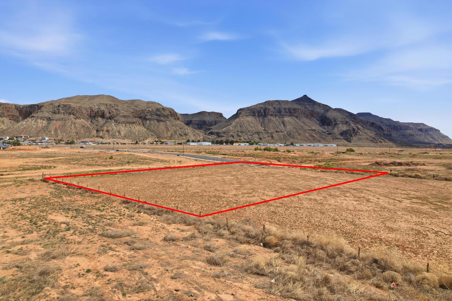 Expansive land parcel featuring natural desert vegetation, partial perimeter fencing, and distant mountain vistas