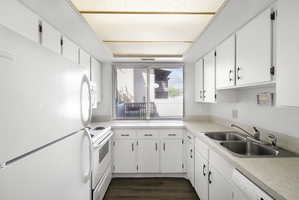 Galley kitchen featuring white cabinetry, light-toned countertops, a double basin stainless steel sink, and wood-finish flooring