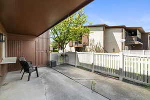 Covered patio featuring a concrete surface, brown vertical siding, a window ledge, and a white picket fence