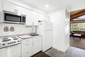 Compact kitchen featuring white cabinetry with brushed nickel hardware, a stainless steel over-the-range microwave, a white electric range, wood-finish flooring, and a white refrigerator