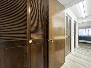 Hallway featuring dark wood bi-fold louvered doors, a light wood-finish flooring, and white painted walls