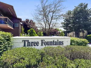 Brick sign with "Three Fountains" lettering, surrounded by varied green foliage