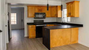 Kitchen featuring wood-finish cabinetry, dark countertops, black appliances, a counter-height bar, and pendant lighting