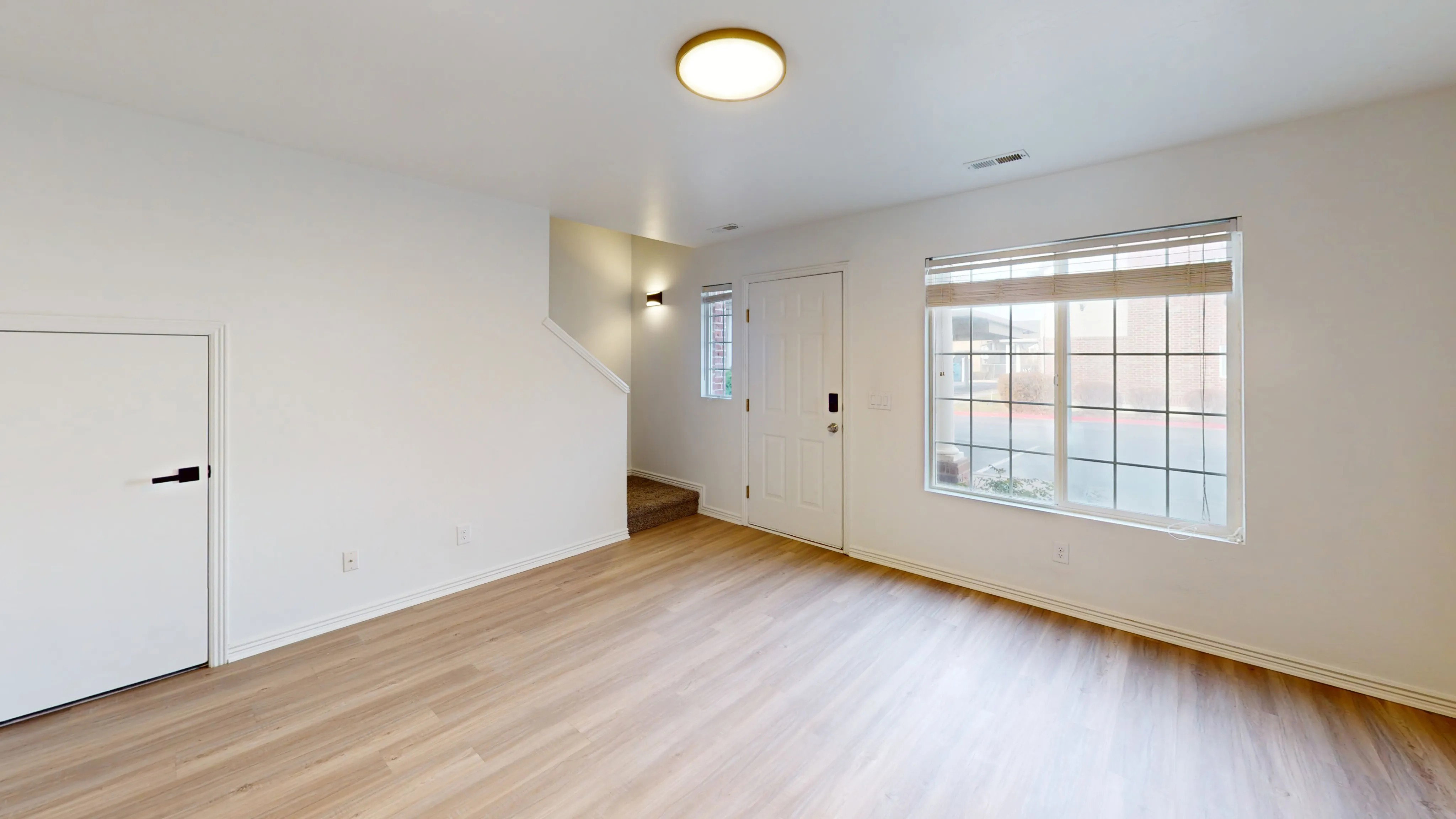 Bright living area featuring wood-finish flooring, white walls, and a large window with white muntins