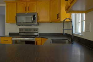 Kitchen featuring dark countertops, a stainless steel sink with a black high-arc faucet, honey-toned cabinetry, and a window providing natural light