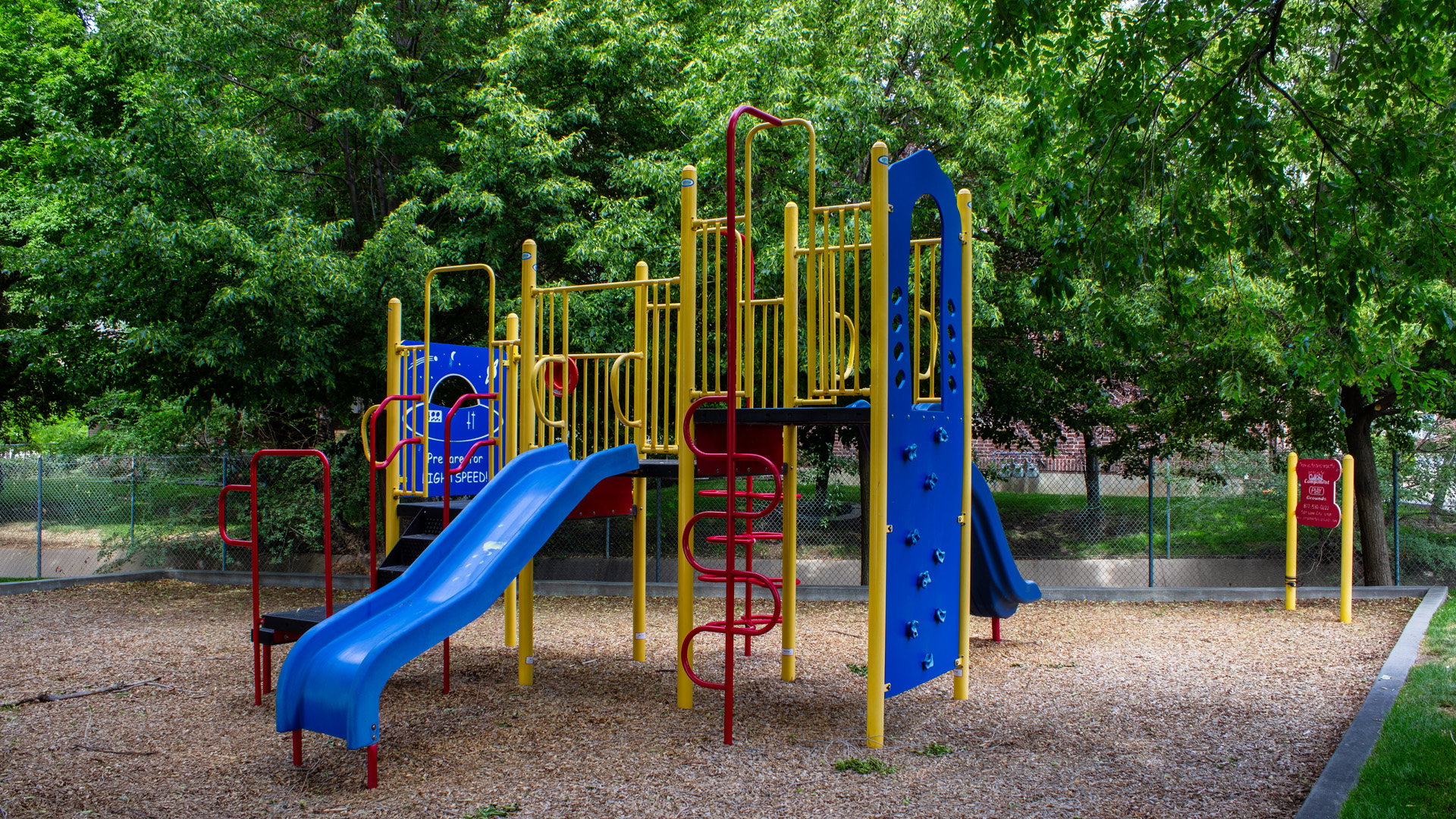 Outdoor play area featuring a multi-level playset with blue slides, yellow and red accents, and climbing elements