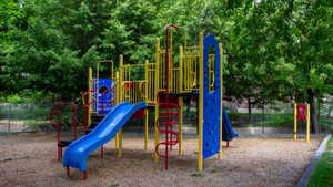 Outdoor play area featuring a multi-level playset with blue slides, yellow and red accents, and climbing elements