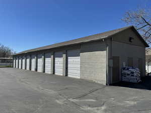 Self-storage facility featuring multiple roll-up garage doors, concrete block construction, a sloped shingle roof, and a paved asphalt drive