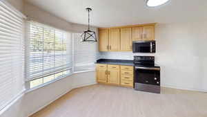 Kitchen area with light wood-finish cabinetry, dark countertops, and black appliances