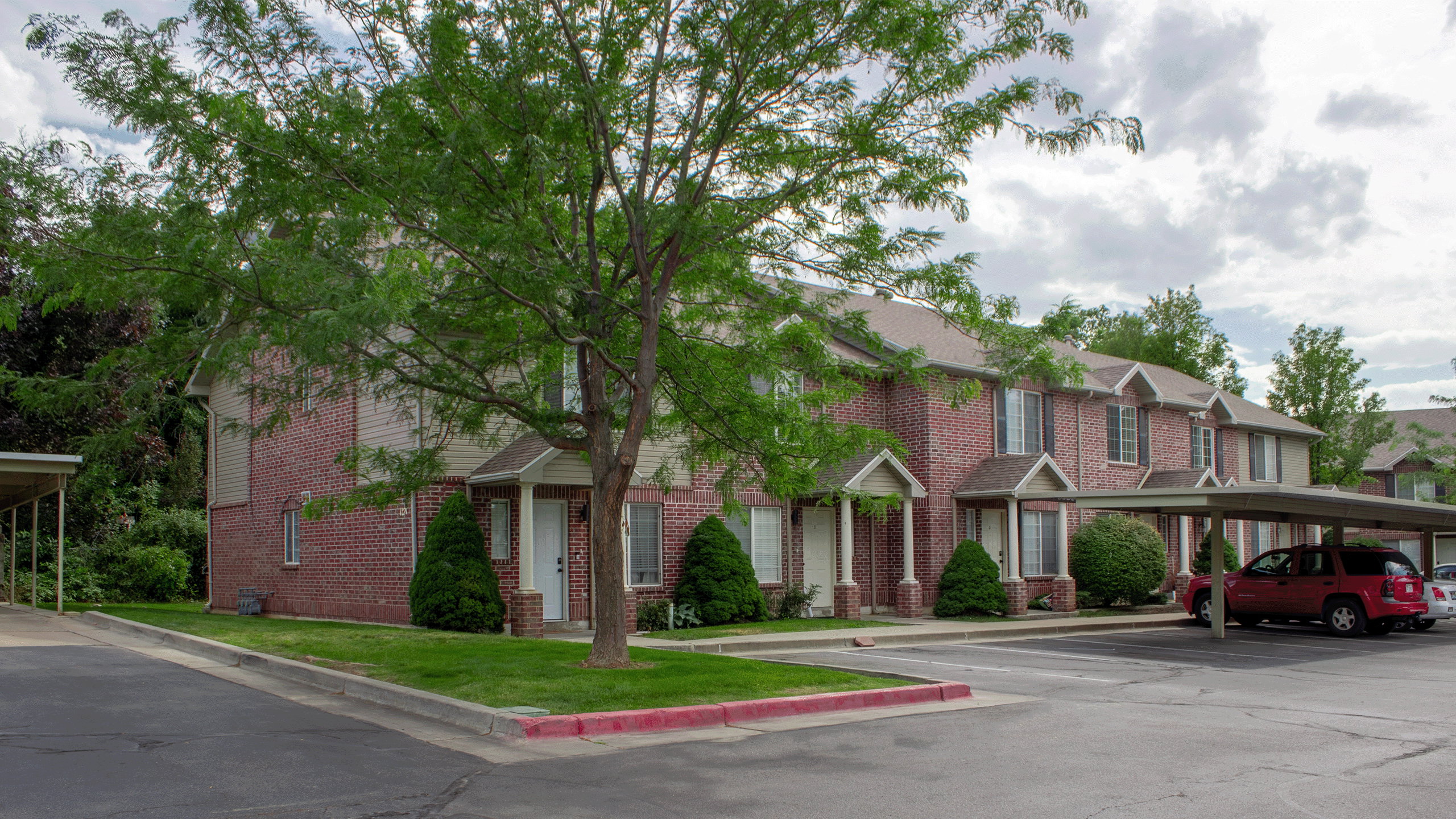 Brick exterior townhome with covered entryways and a mature tree providing shade