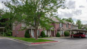 Brick exterior townhome with covered entryways and a mature tree providing shade
