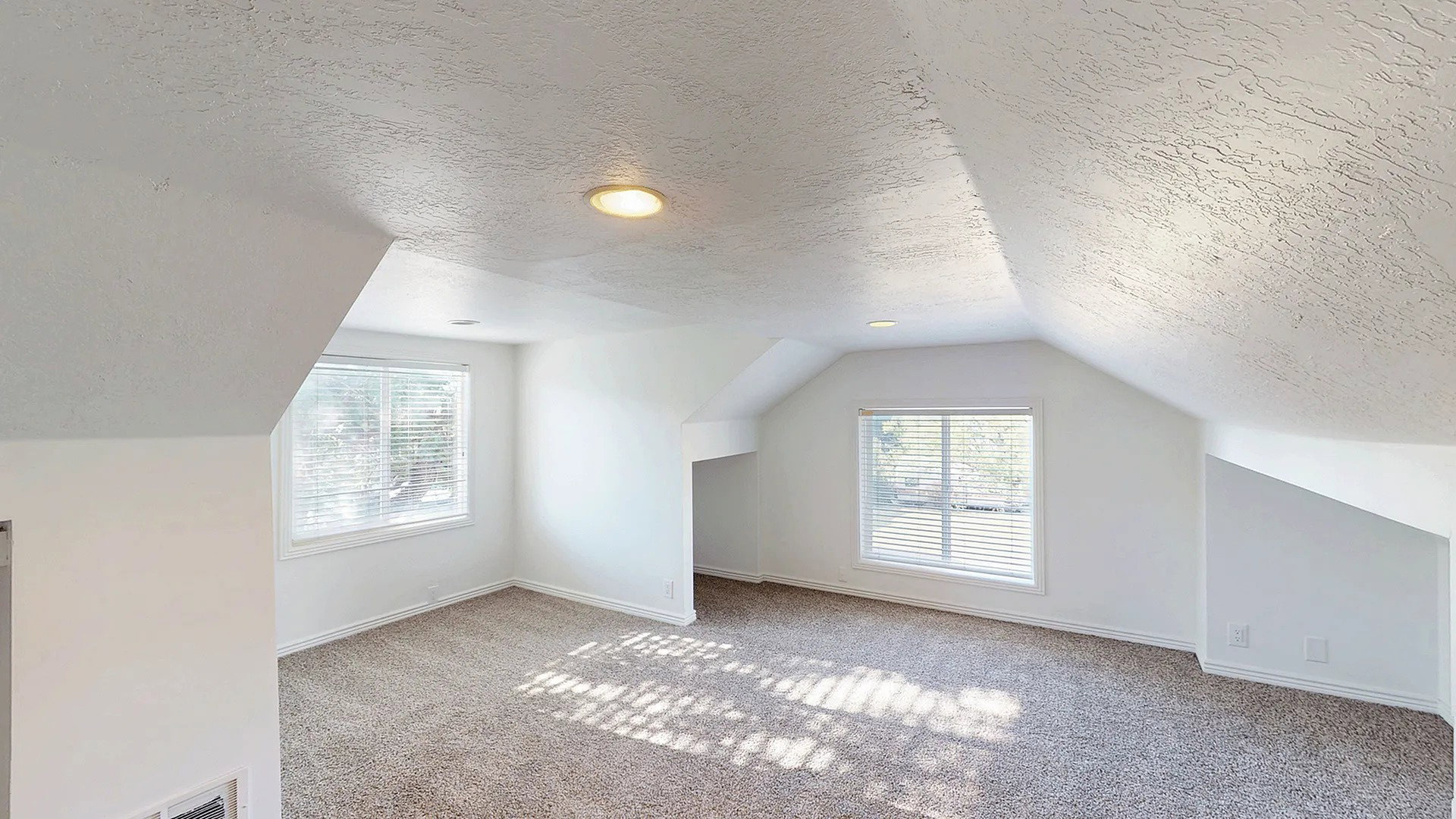 Spacious room featuring sloped ceilings, two windows with blinds, recessed lighting, and neutral-toned carpeting