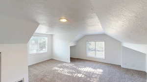 Spacious room featuring sloped ceilings, two windows with blinds, recessed lighting, and neutral-toned carpeting