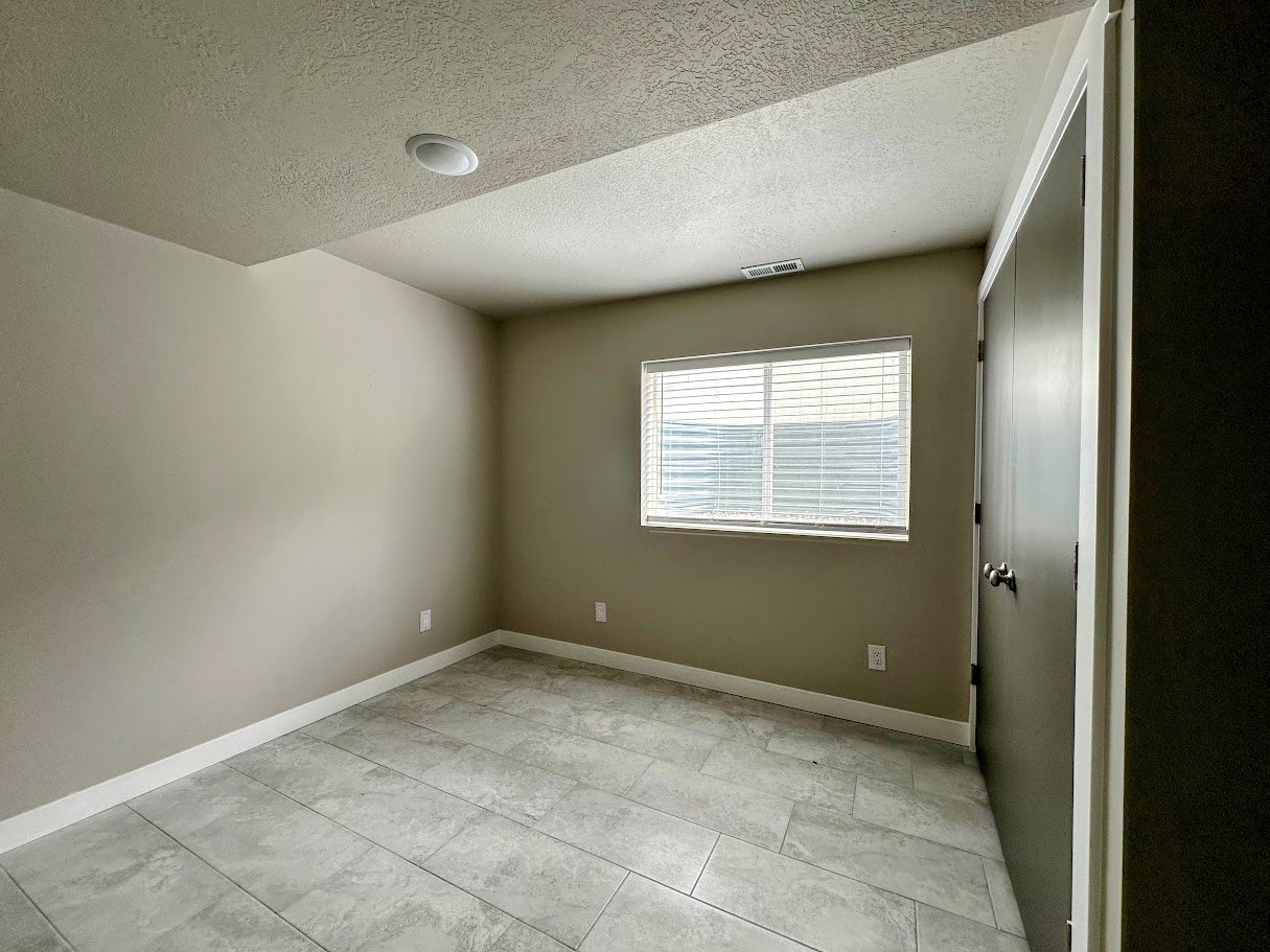 Spacious room featuring tile flooring, neutral wall paint, a window with blinds, recessed lighting, and a dark-paneled closet