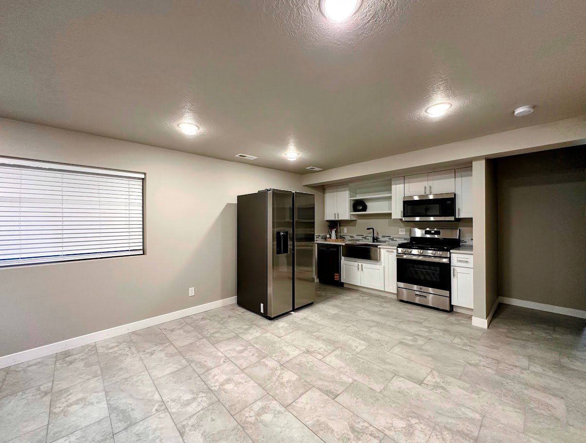 Contemporary kitchen featuring stainless steel appliances, white cabinetry, a tile backsplash, and light-toned tile flooring