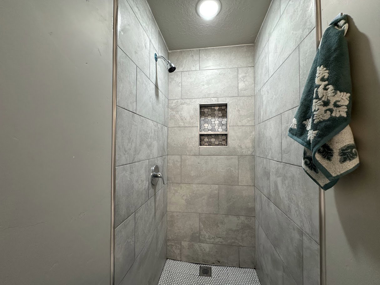 Shower stall with light grey rectangular tile walls and a white hex tile floor