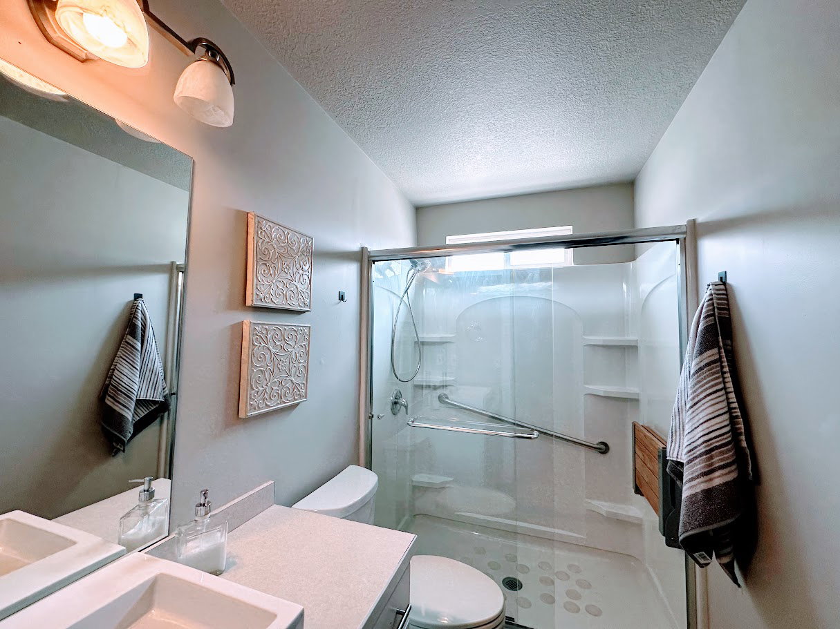 Contemporary bathroom featuring a dual-sink vanity with a light-toned countertop, a frameless mirror, and an enclosed shower with a clear glass door