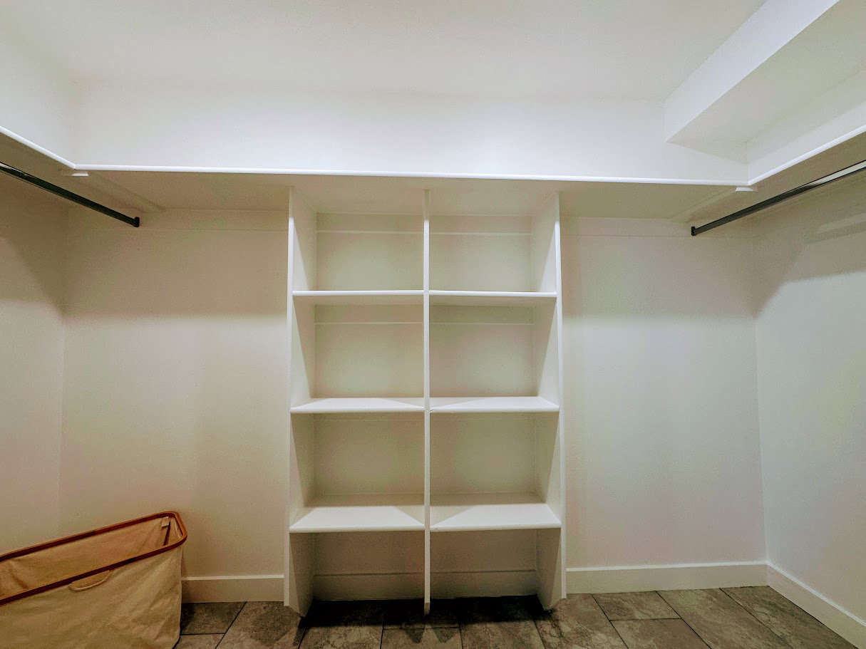 Walk-in closet featuring white built-in shelving, two hanging rods, white walls, and stone-finish flooring