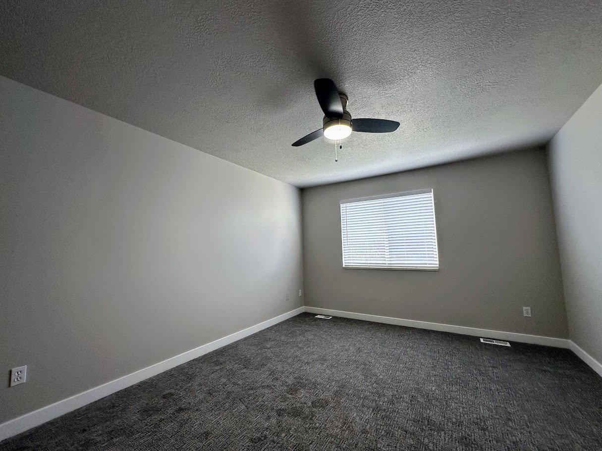 Spacious room featuring neutral painted walls, textured ceiling, and dark patterned carpet