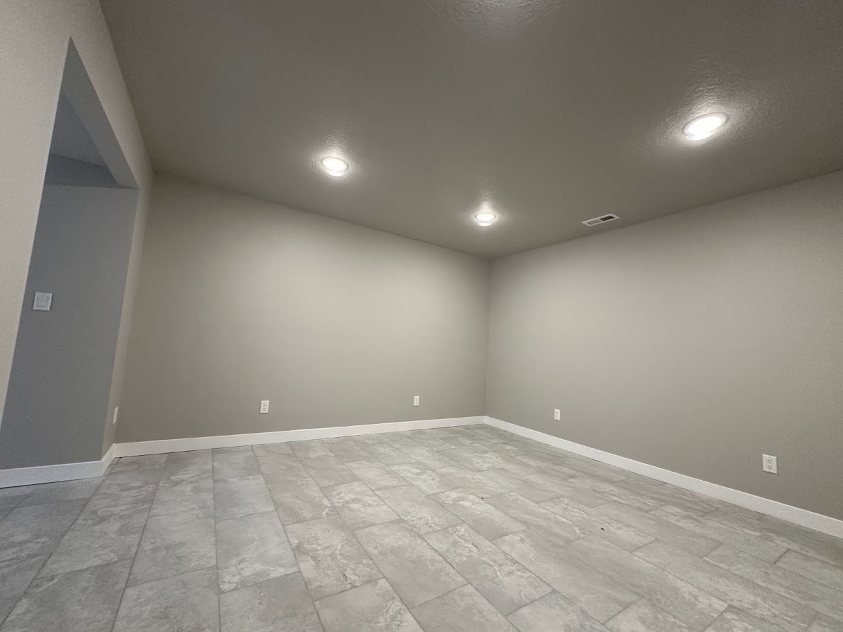 Spacious interior room featuring light gray walls, large format tile flooring, white baseboards, and recessed ceiling lighting