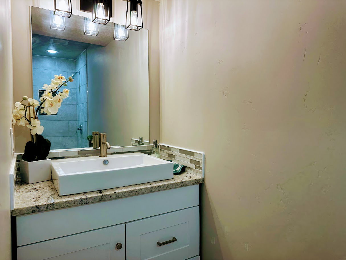 White rectangular vessel sink with a brushed brass faucet, set on a granite countertop with a mosaic tile backsplash