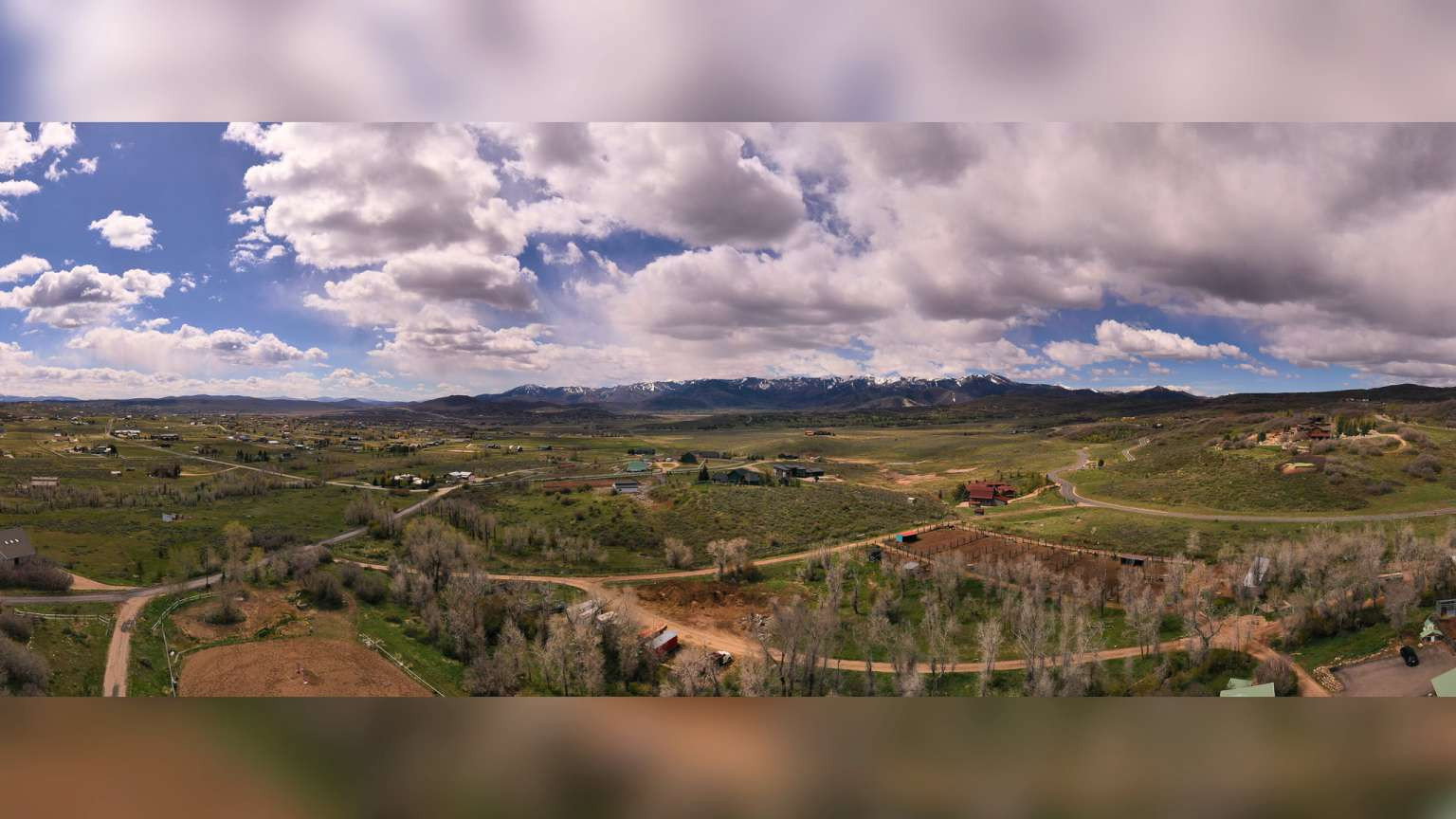 Expansive rural landscape featuring distant snow-capped mountains and scattered residential structures