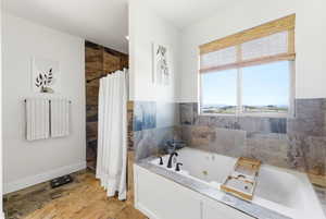 Full bath featuring stone tile flooring, a jetted tub, and tiled shower