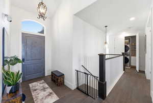 Foyer featuring dark wood-type flooring, stacked washing machine and dryer, hanging lights, and vaulted ceiling