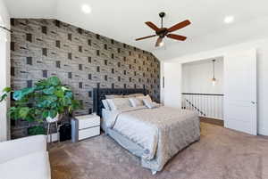 Carpeted bedroom featuring an accent wall, lofted ceiling, wallpapered walls, and a ceiling fan
