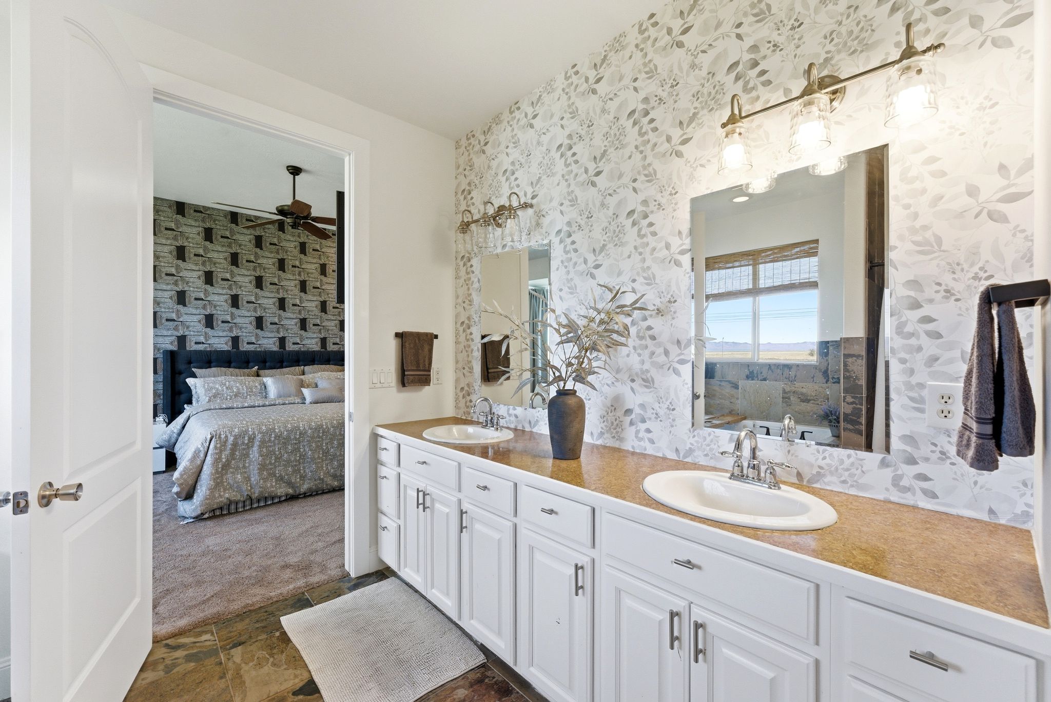 Ensuite bathroom with double vanity, dark stone finish flooring, wallpapered walls, and a ceiling fan
