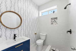 Full bathroom featuring vanity, tiled shower, and wallpapered walls