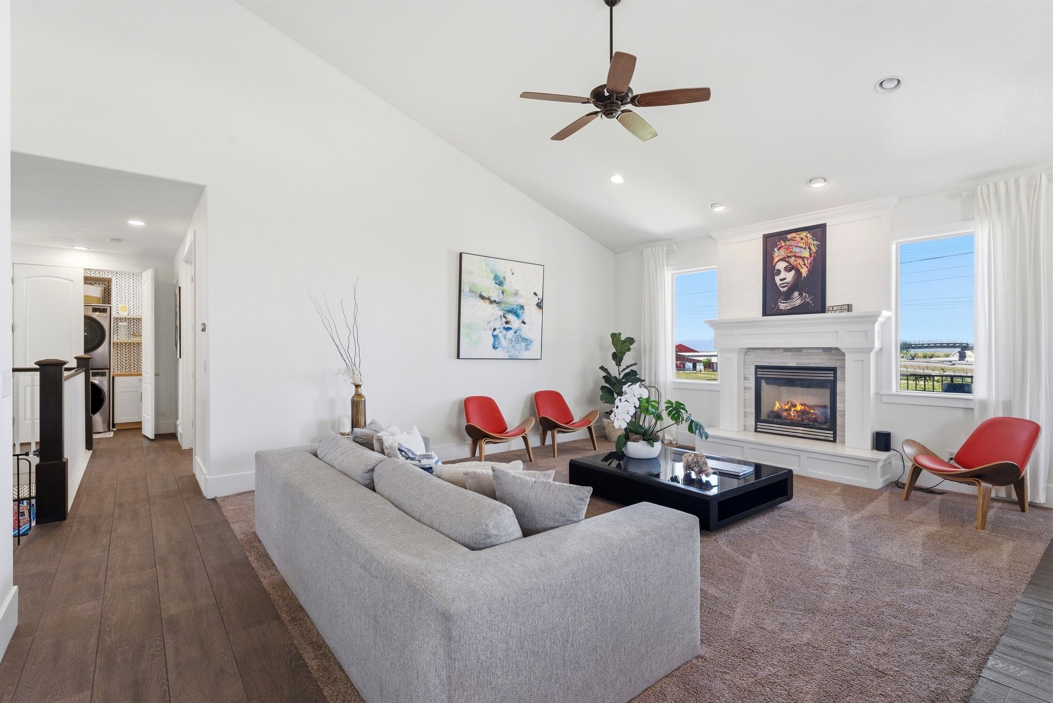 Living room with stacked washer / drying machine, dark wood finished floors, ceiling fan, healthy amount of natural light, and lofted ceiling