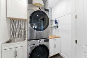 Laundry area featuring cabinet space, stacked washer and clothes dryer, and dark wood-type flooring