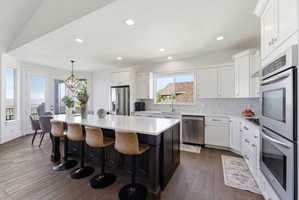 Kitchen with dark wood-style flooring, stainless steel appliances, a kitchen island, two tone cabinetry, and a breakfast bar